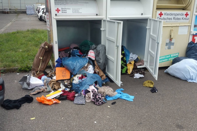 Zwei aufgebrochene Altkleidercontainer. Der Inhalt wurde durchwühlt und liegt verteilt herum.
